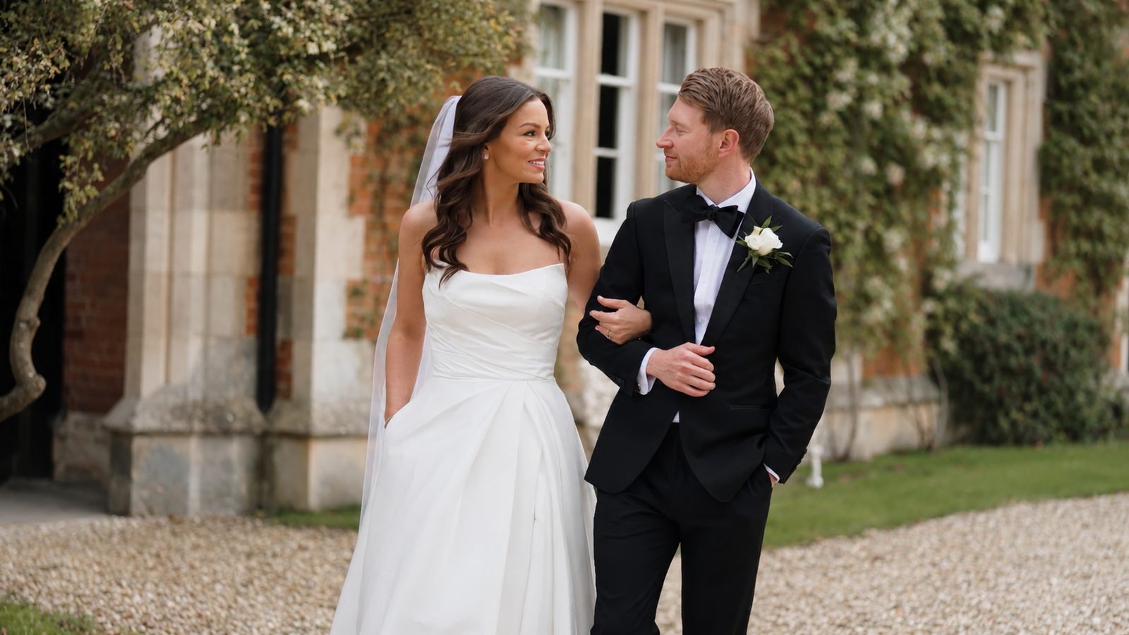 Couple in black tie walking arm in arm outside an ivy-covered hall